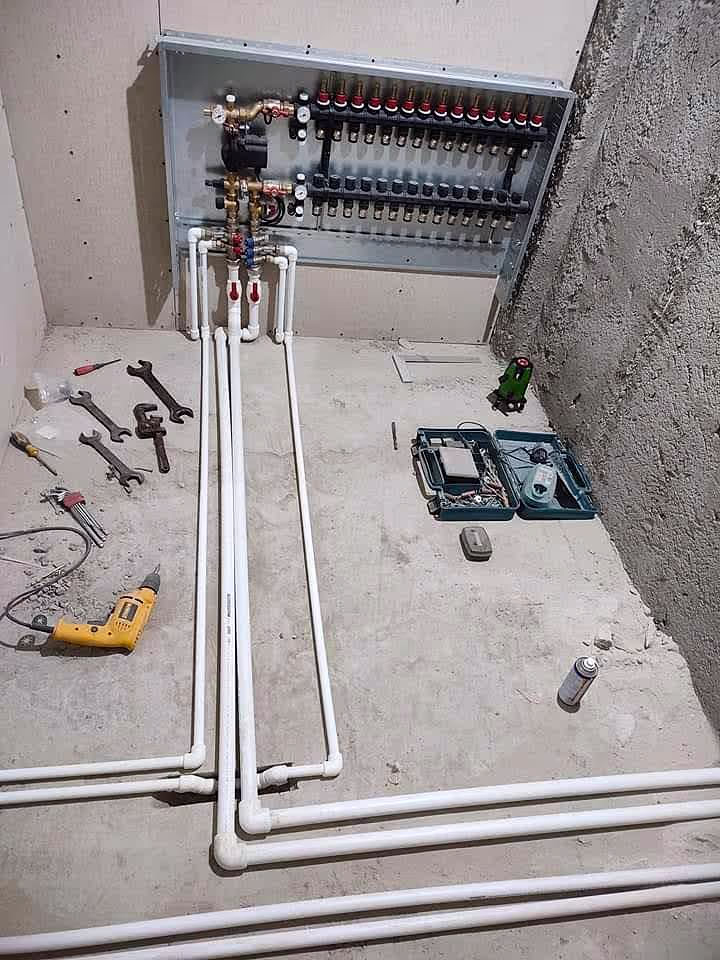 An installation of a heating manifold system with white PVC pipes laid out on a concrete floor, along with various tools and equipment.