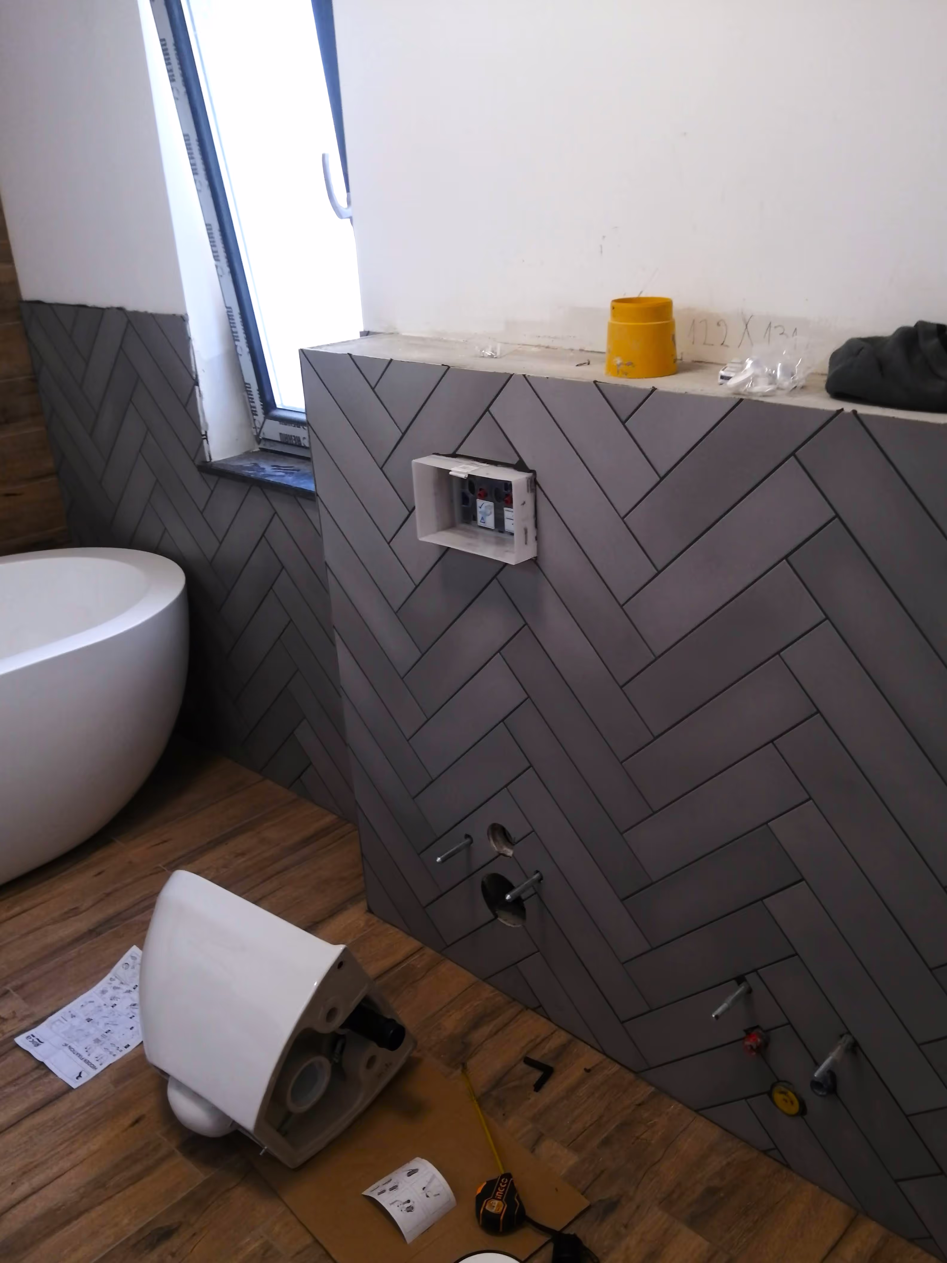 A partially installed bathroom with a wall-mounted toilet frame, a freestanding bathtub, and exposed plumbing connections.