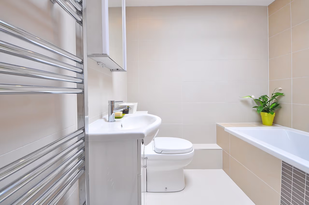 Modern bathroom installation with a white sink, toilet, bathtub, and a chrome towel radiator in a bright tiled space.
